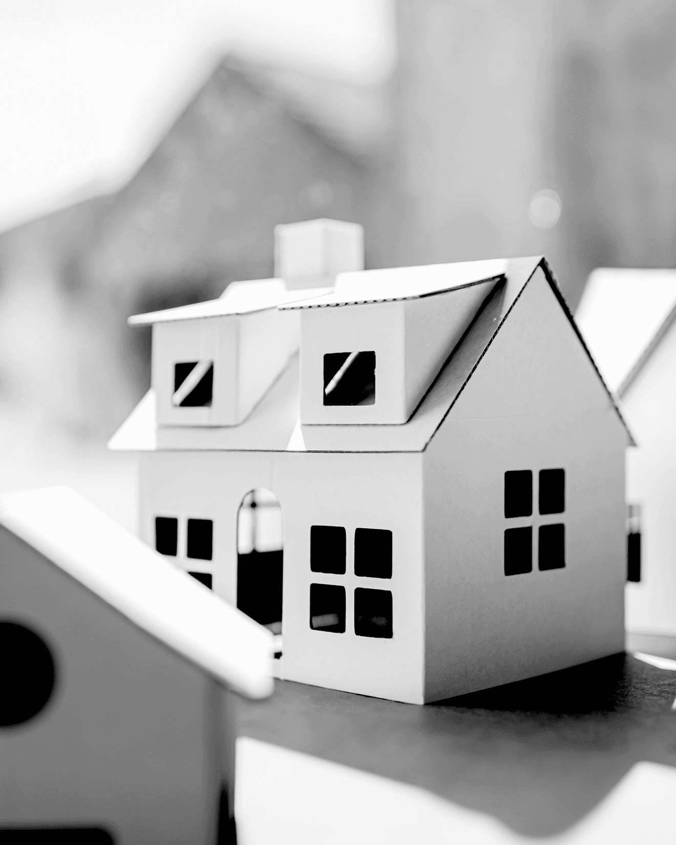 Two-story paper model house with gabled roof, dormer windows, and arched doorway, shown in black and white.