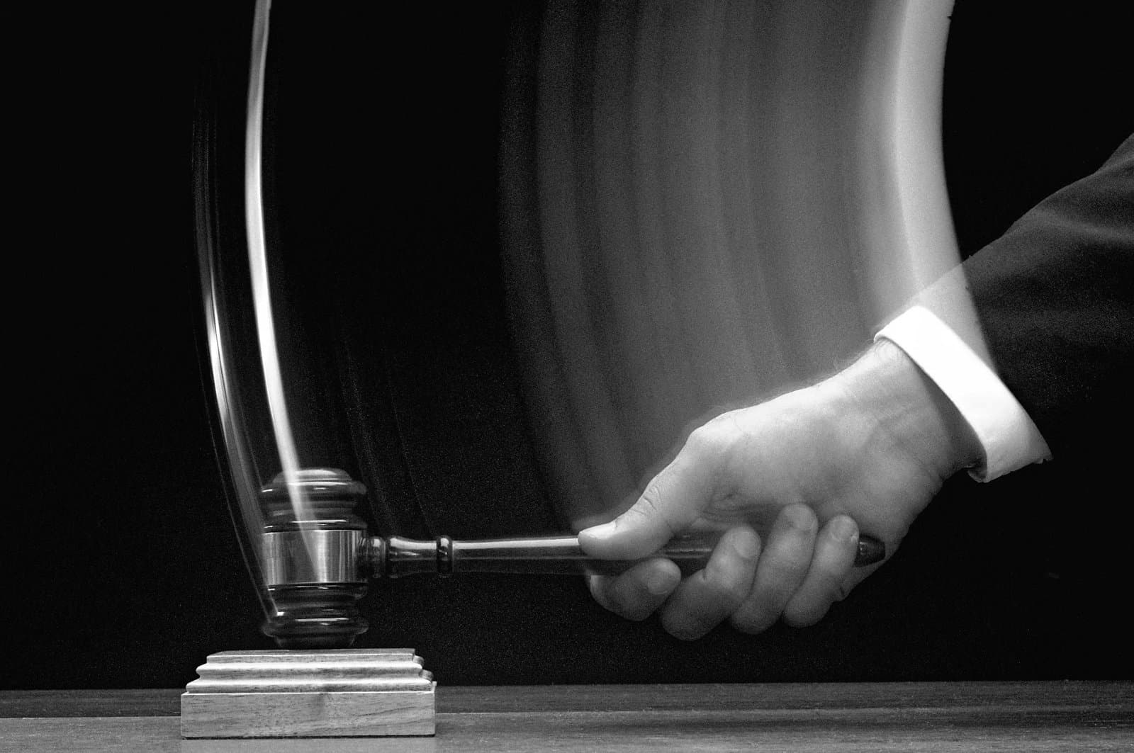 A hand striking a wooden gavel down onto a sound block.