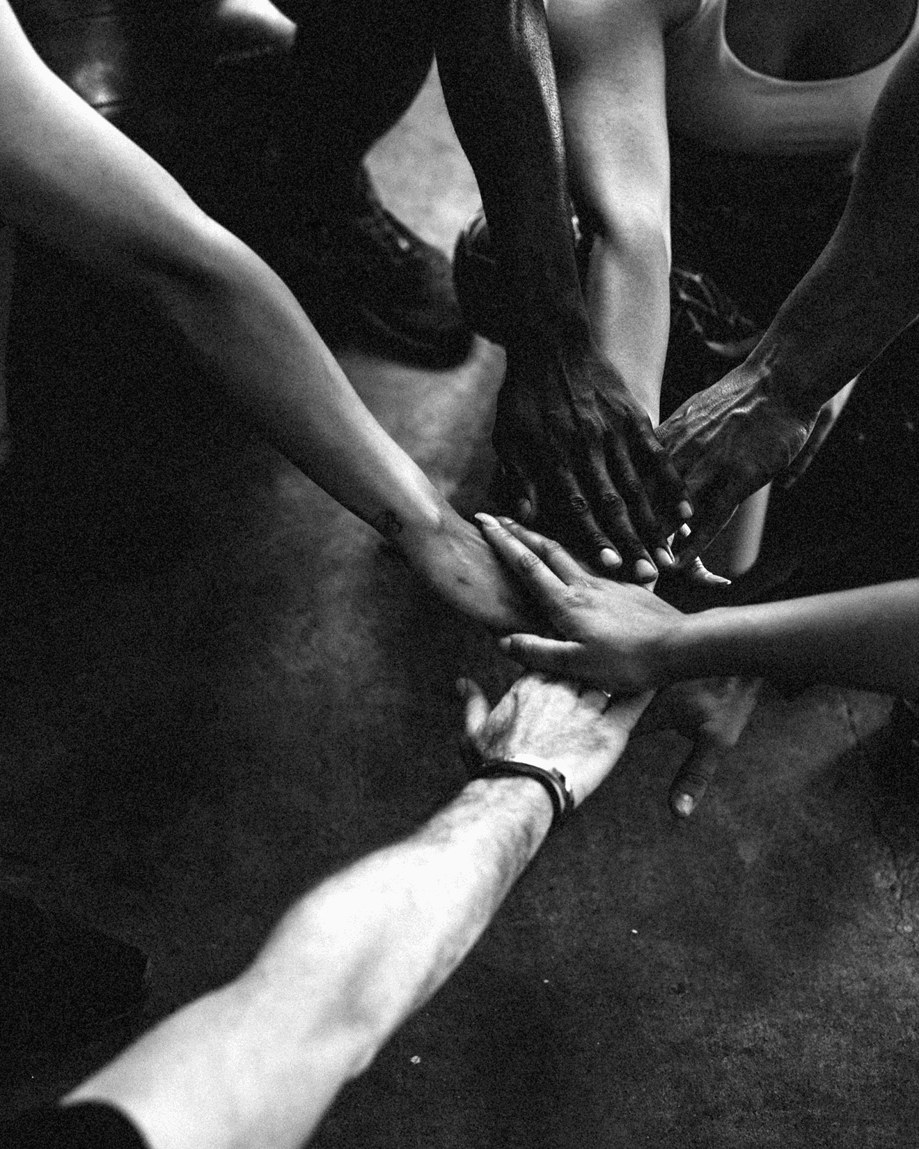 Six hands stacked in the center, showing diverse skin tones and blurred background.