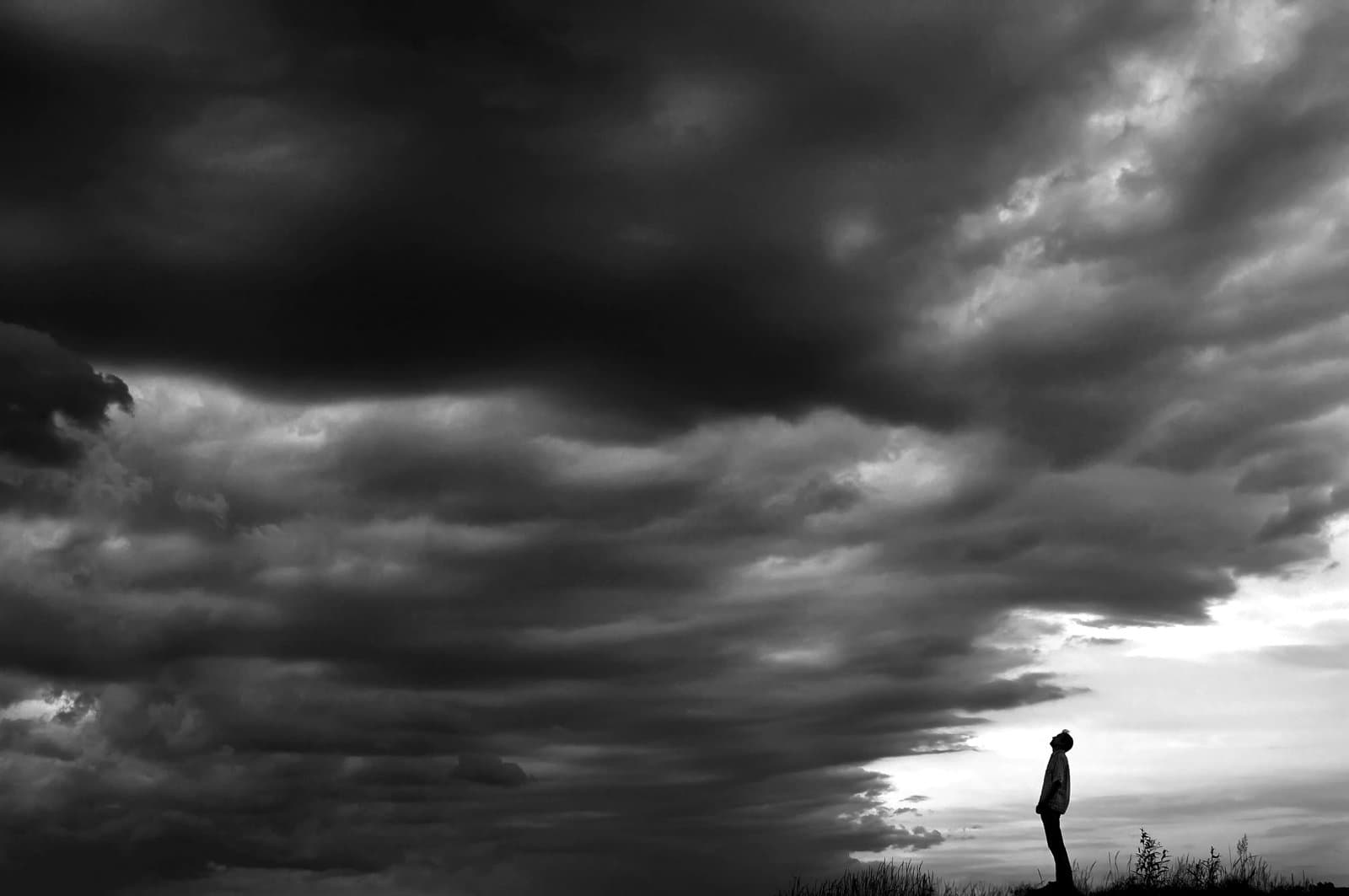 A lone person standing under a dramatic sky filled with dark, heavy storm clouds.